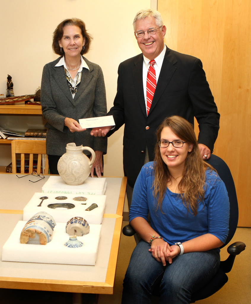 Julia King, associate professor of anthropology, is presented with a donation by James J. Winn Jr., governor of the Society for Colonial Wars. Exhibit creator Jessy Schroeder is seated in front.