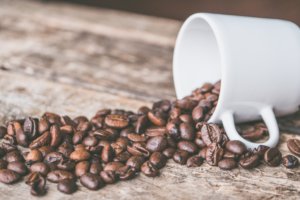 white coffee mug tipped over, spilling out fresh coffee beans on wooden table