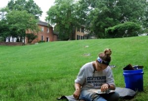 female student sitting outside on the grass reading a book