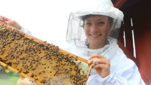 SMCM student in beekeeping suit holding up a honeycomb