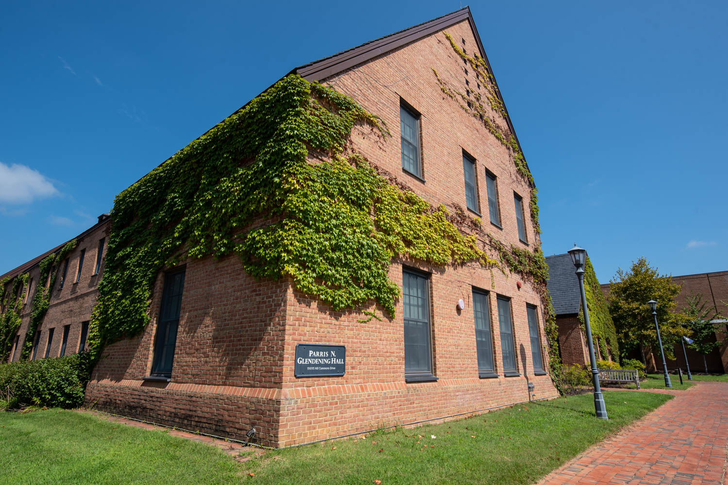 A two-story brick building with ivy growing on the side, set against a clear blue sky. To the right, a brick path leads through a grassy area. A sign on the building reads "Parris N. Glendening Hall.