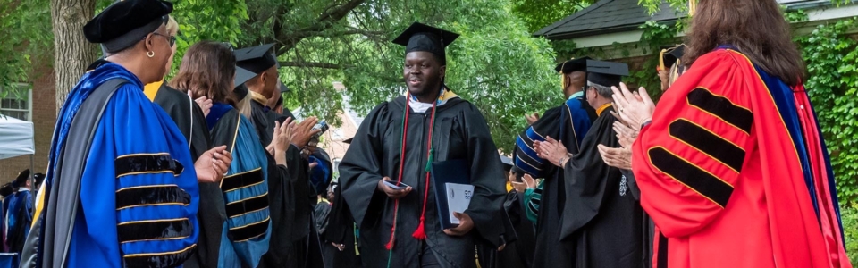 A graduate walks through the receiving line with the president, board and faculty clapping their hands congratulating him.