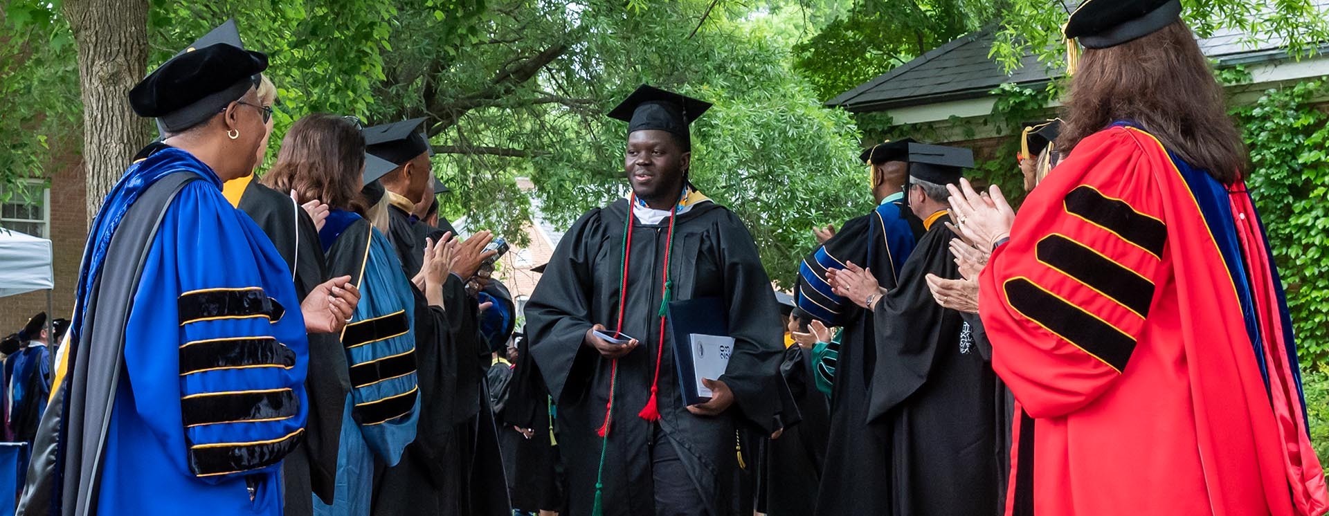 A graduate walks through the receiving line with the president, board and faculty clapping their hands congratulating him.